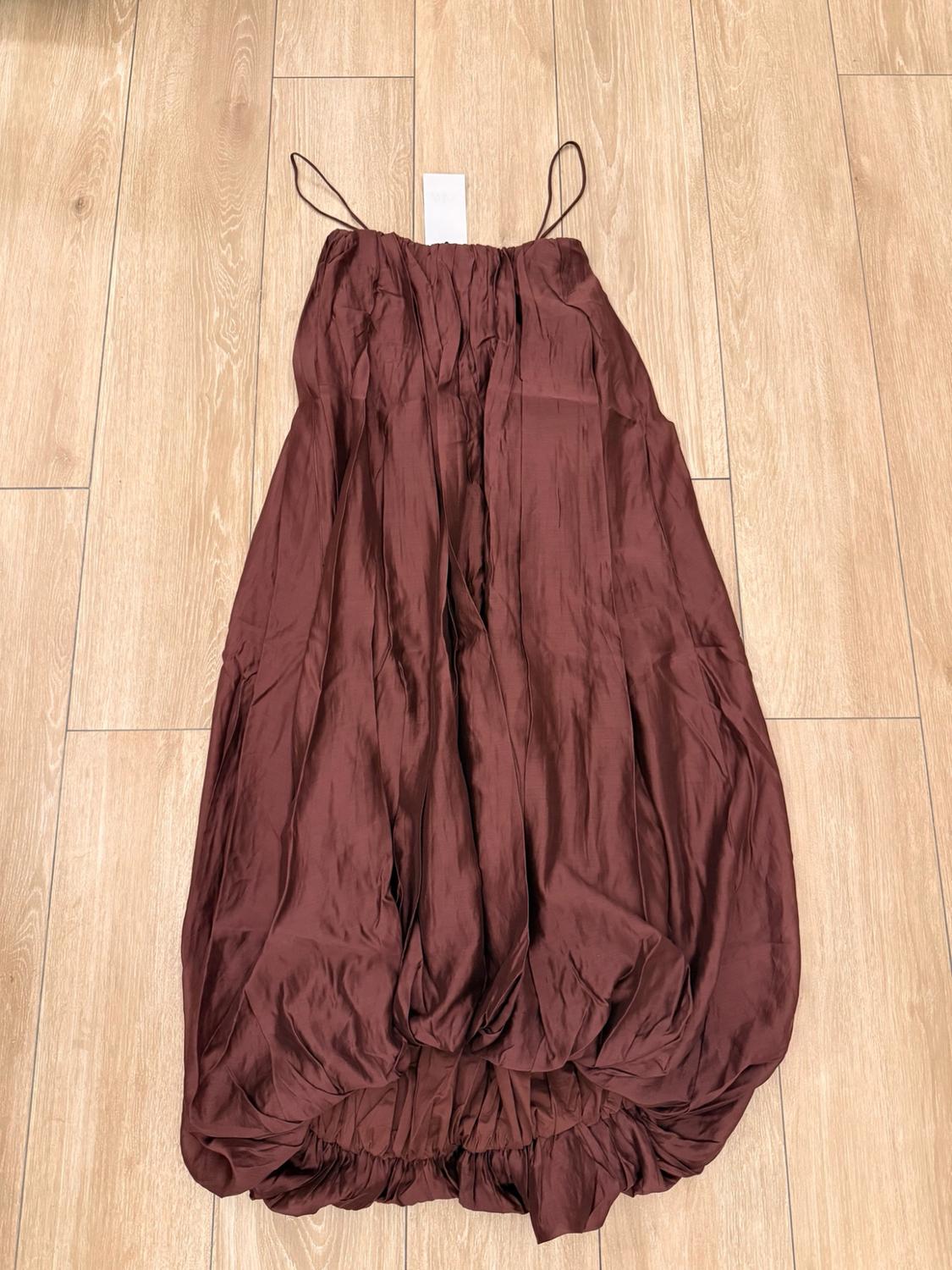 Burgundy dress with thin straps, a ruched straight neckline and a puffed hem, laid out on a light wooden floor.