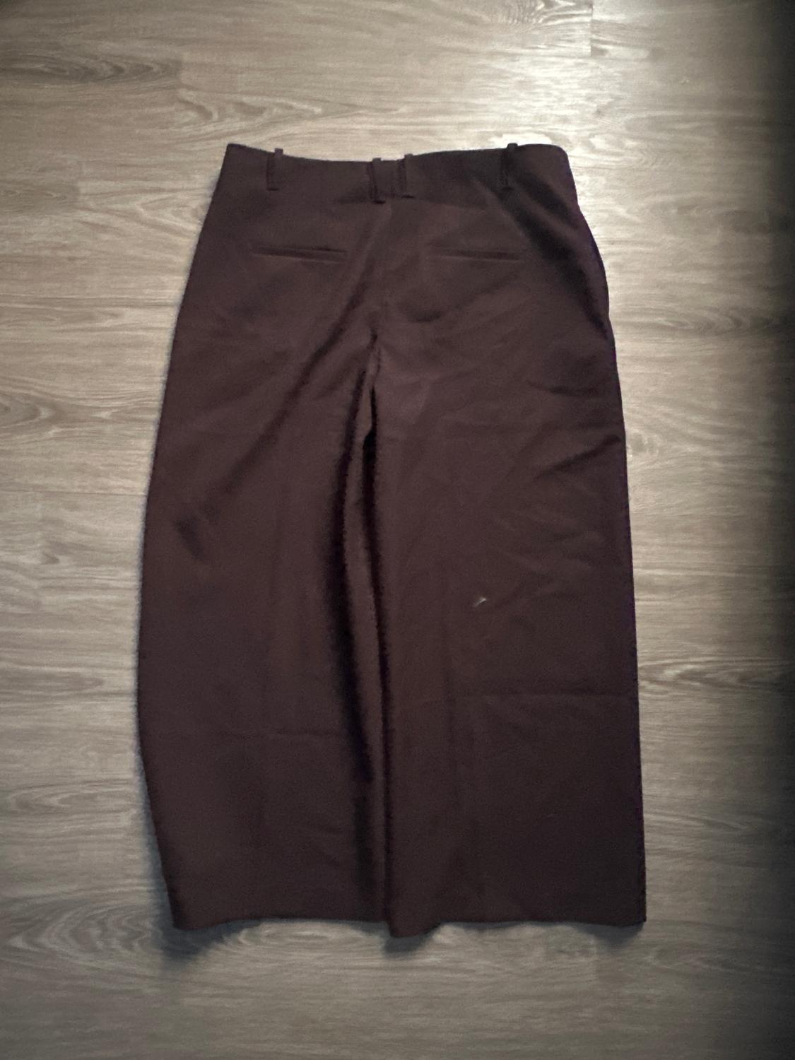 Brown dress pants on a light wooden floor. The garment is laid out, showcasing its classic design and back pockets.