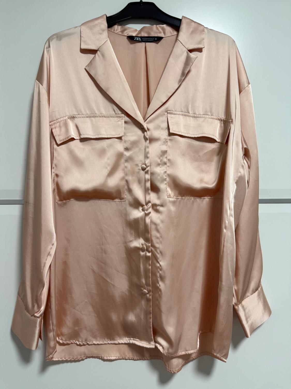 Light pink satin shirt with front pockets and matching buttons, hanging on a black hanger.