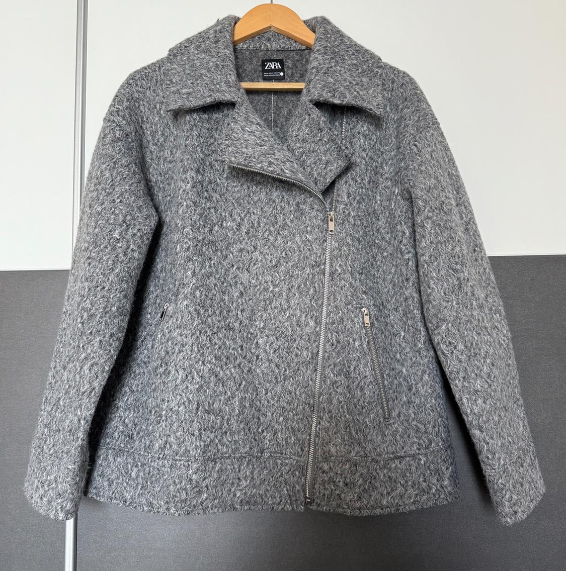 Grey wool jacket with asymmetric zip and wide collar, hanging on a wooden coat hanger. Visible label: Zara.