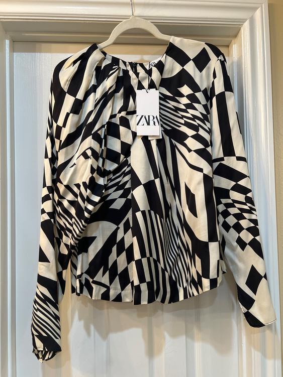 Hanging blouse with black and white geometric print, visible label with the text "ZARA", white door background.