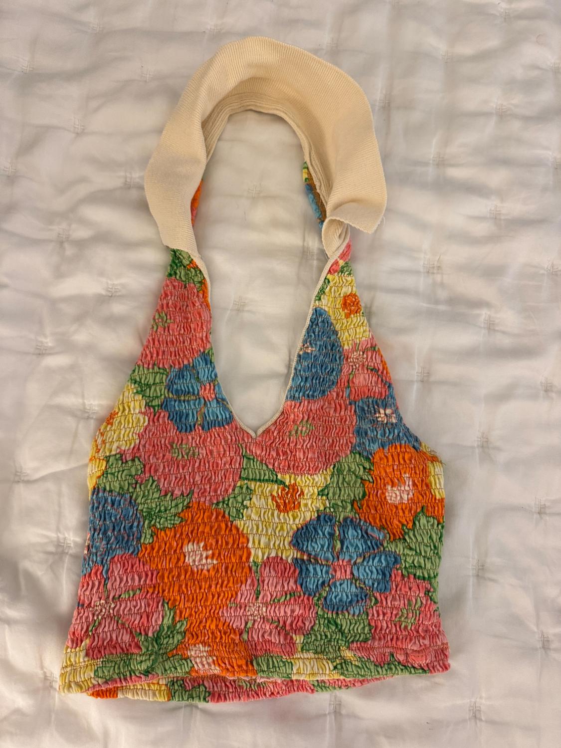 Halter neck top with multicoloured floral print in shades of orange, pink, blue and green, on gathered fabric, padded white background.