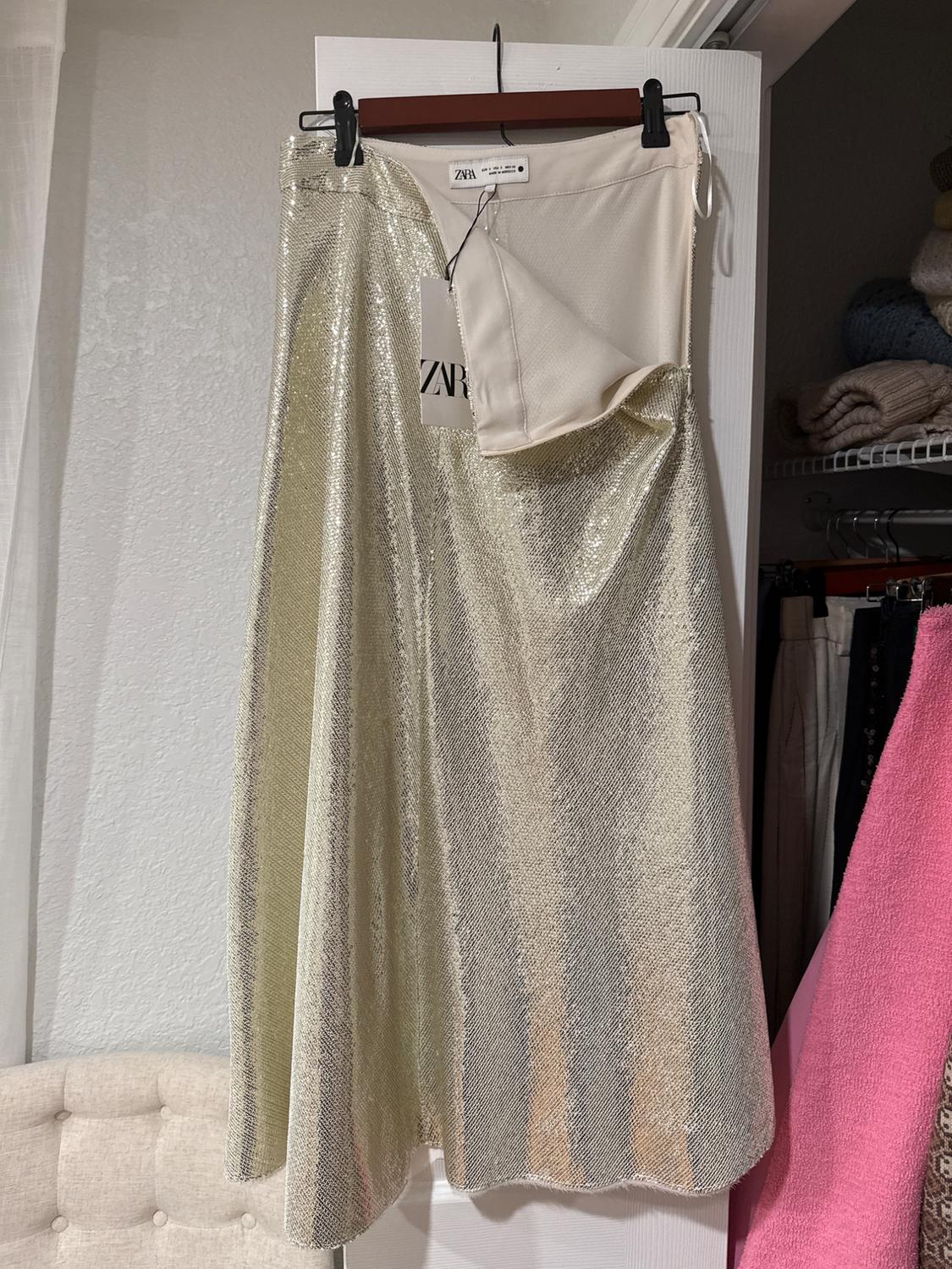Shiny golden skirt hanging on a hanger with a visible tag. Closet background with folded clothes and a beige chair.