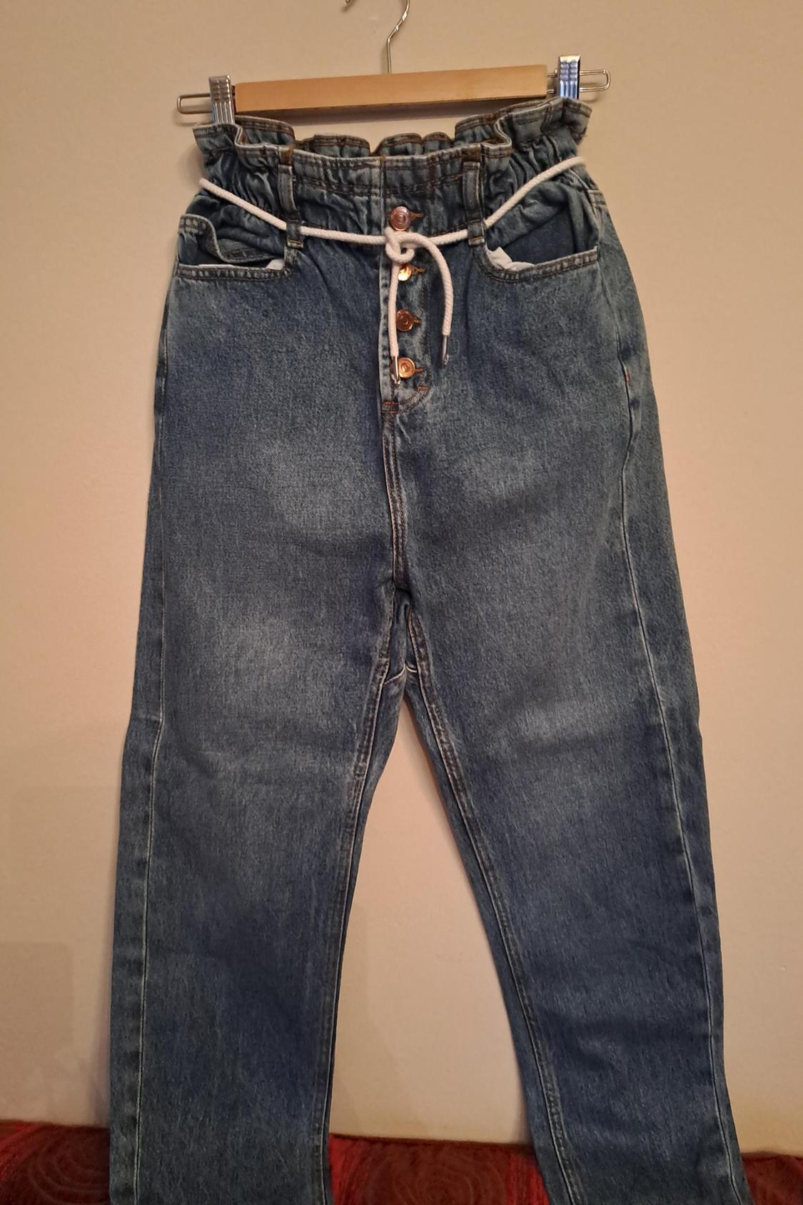 Front view of blue denim jeans with elasticated waistband and drawstring, side pockets and visible button fastening.