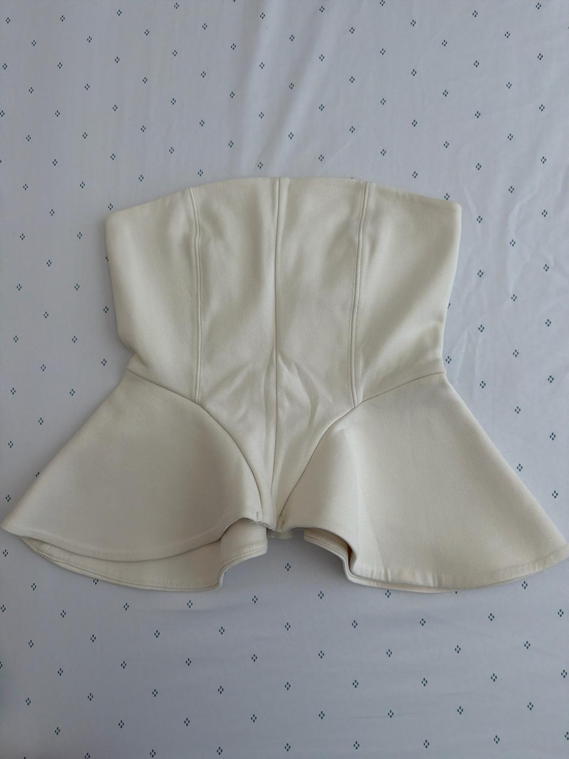 White strapless top with a peplum hem, photographed on white fabric with a subtle pattern of small dark diamonds.