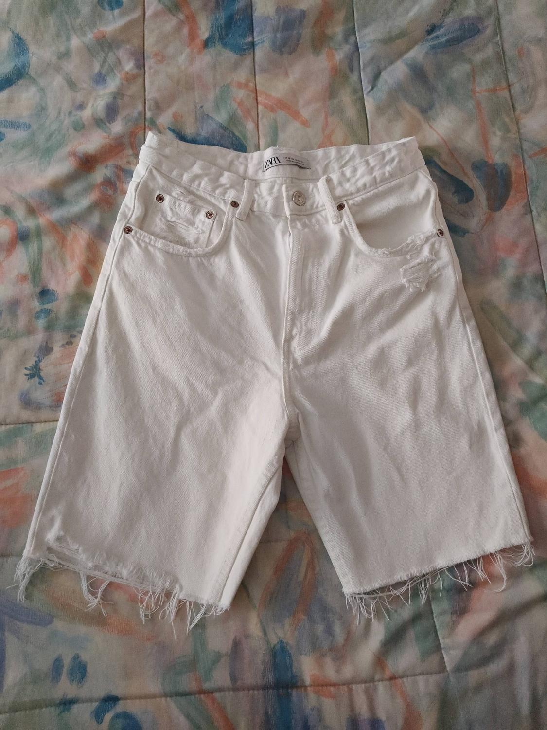 White denim shorts with a frayed hem on a colourful quilt. Visible label on the waistband.