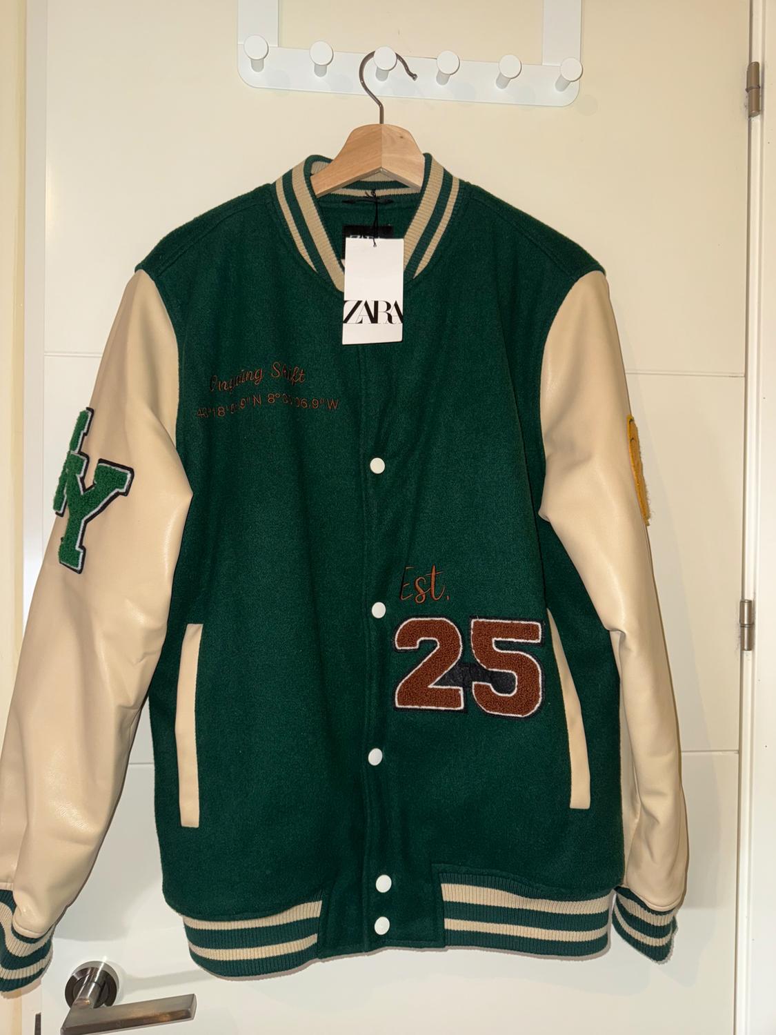 Green varsity jacket with beige sleeves, "Training Shift" and "Est. 25" text on the front. Zara tag hanging.