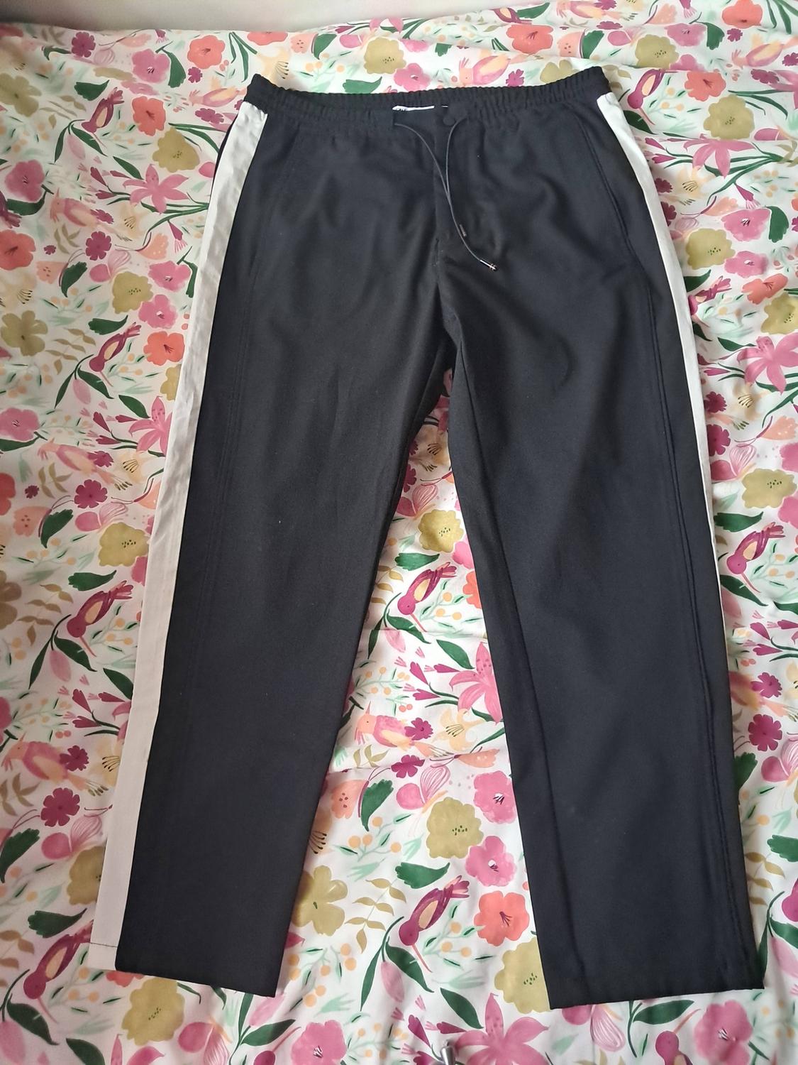 Black tracksuit bottoms with a white stripe down the sides and an adjustable drawstring, laid out on a fabric with a colourful floral print.