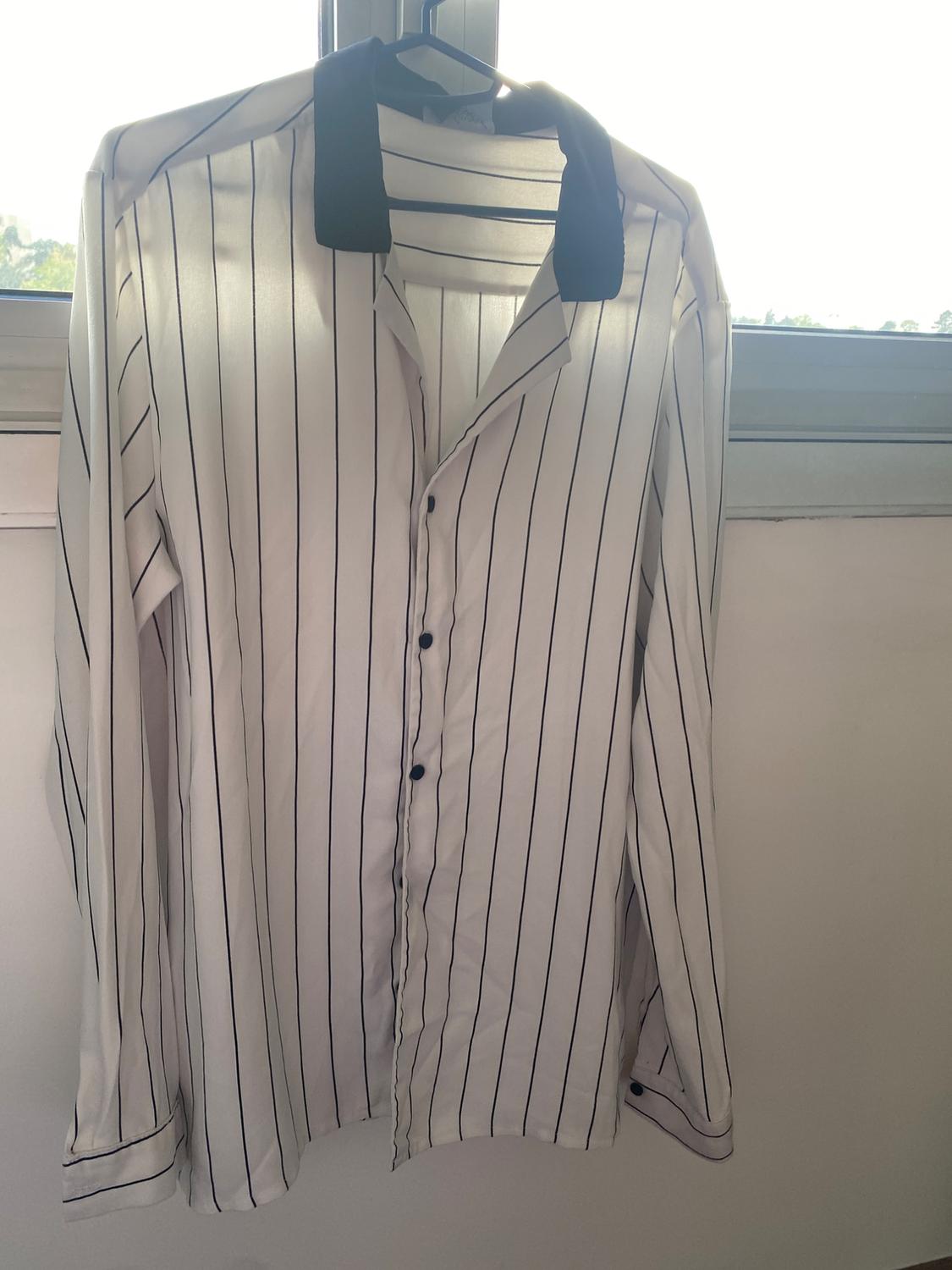 Front view of a white shirt with vertical black stripes and a black collar, long sleeves with buttons.
