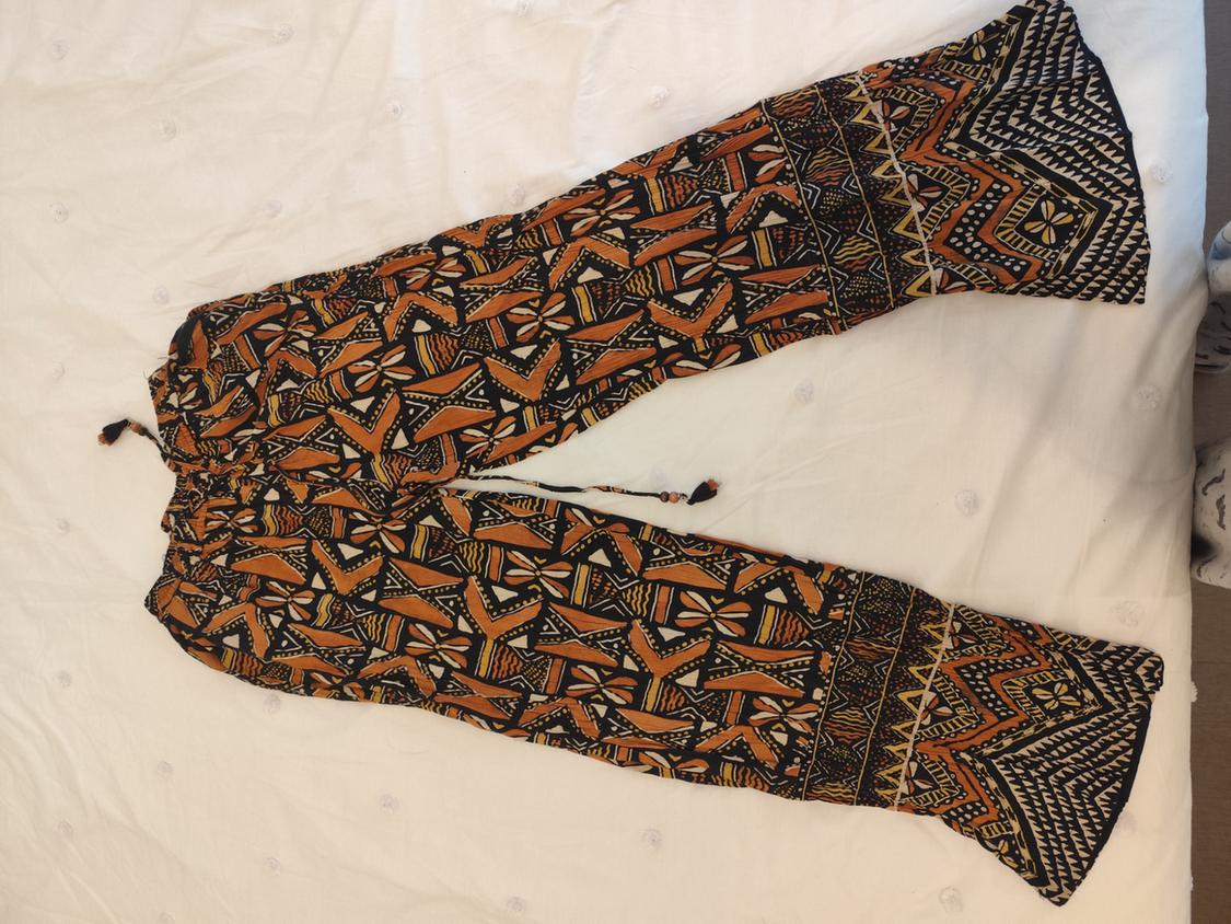 Wide-leg trousers with a geometric print in orange and black tones, on a white padded surface.