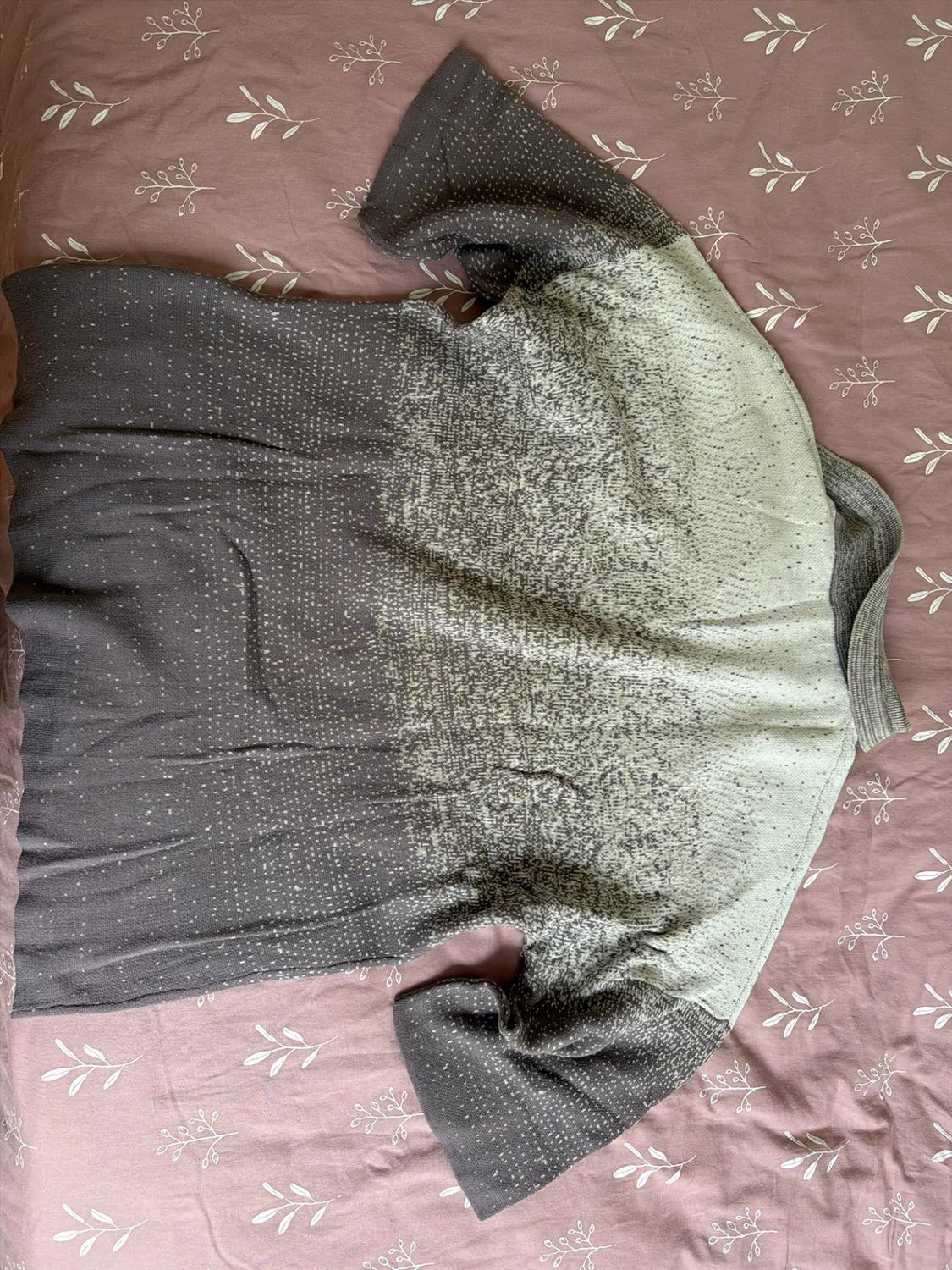 Knit sweater with an ombre effect in shades of gray and cream, on a pink sheet with a leaf print.