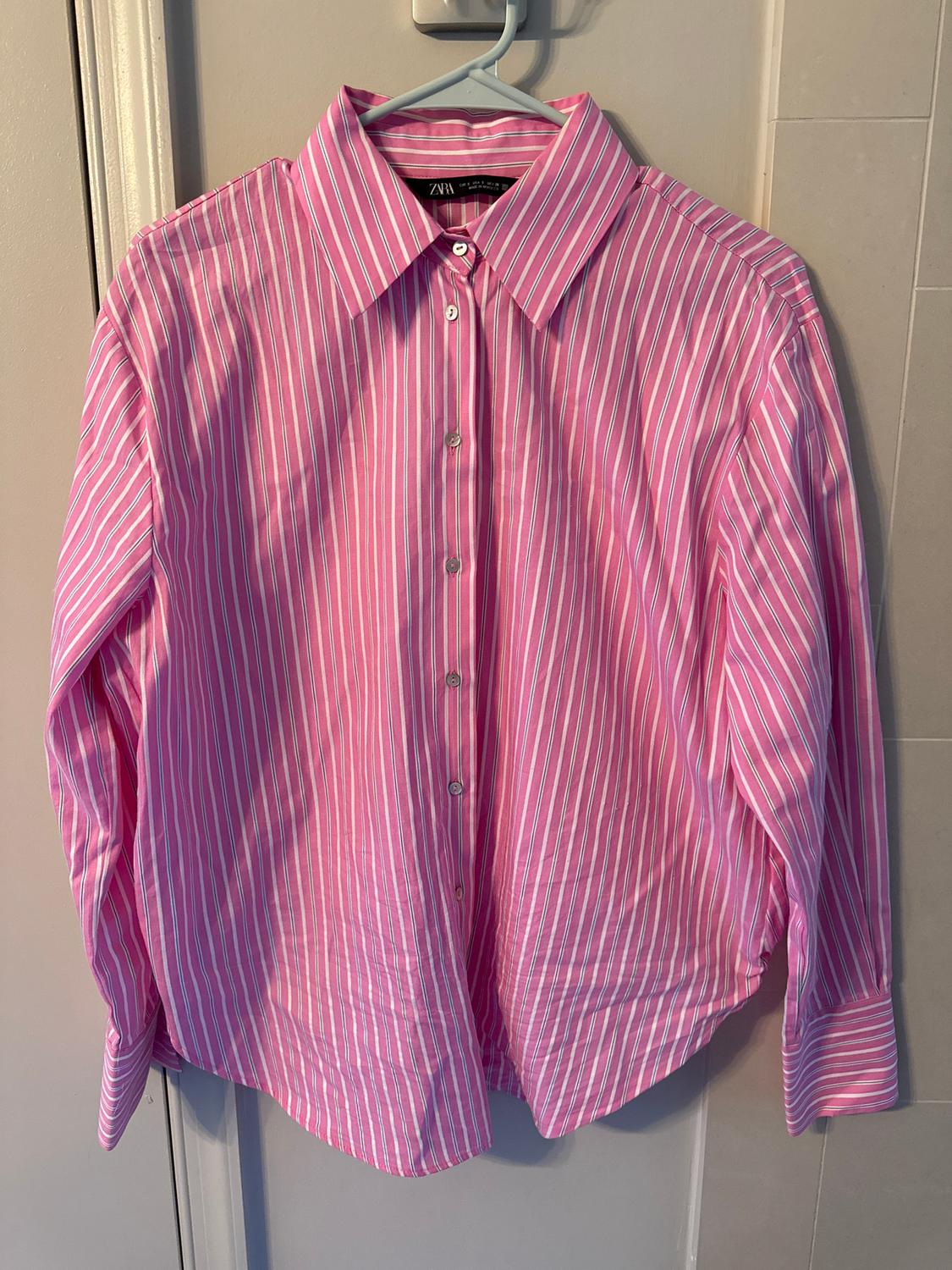 Pink and white striped shirt hanging on a hanger over a door. The label reads "Zara".