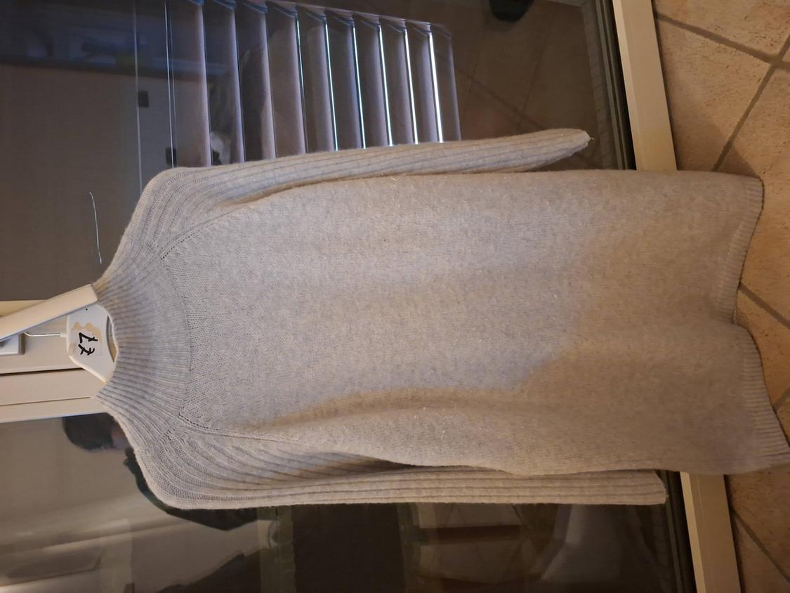 Grey knitted jumper hanging on a white hanger with the number 42, in front of a window with closed blinds.