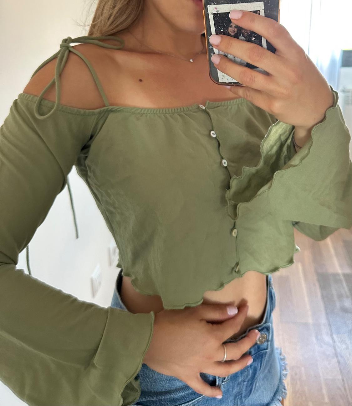 Woman in a green button-up camisole with long, flared sleeves, paired with denim shorts. She's holding a phone.