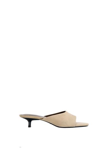 Low-heeled beige shoe on a white background. Minimalist design with an open toe and exposed heel.