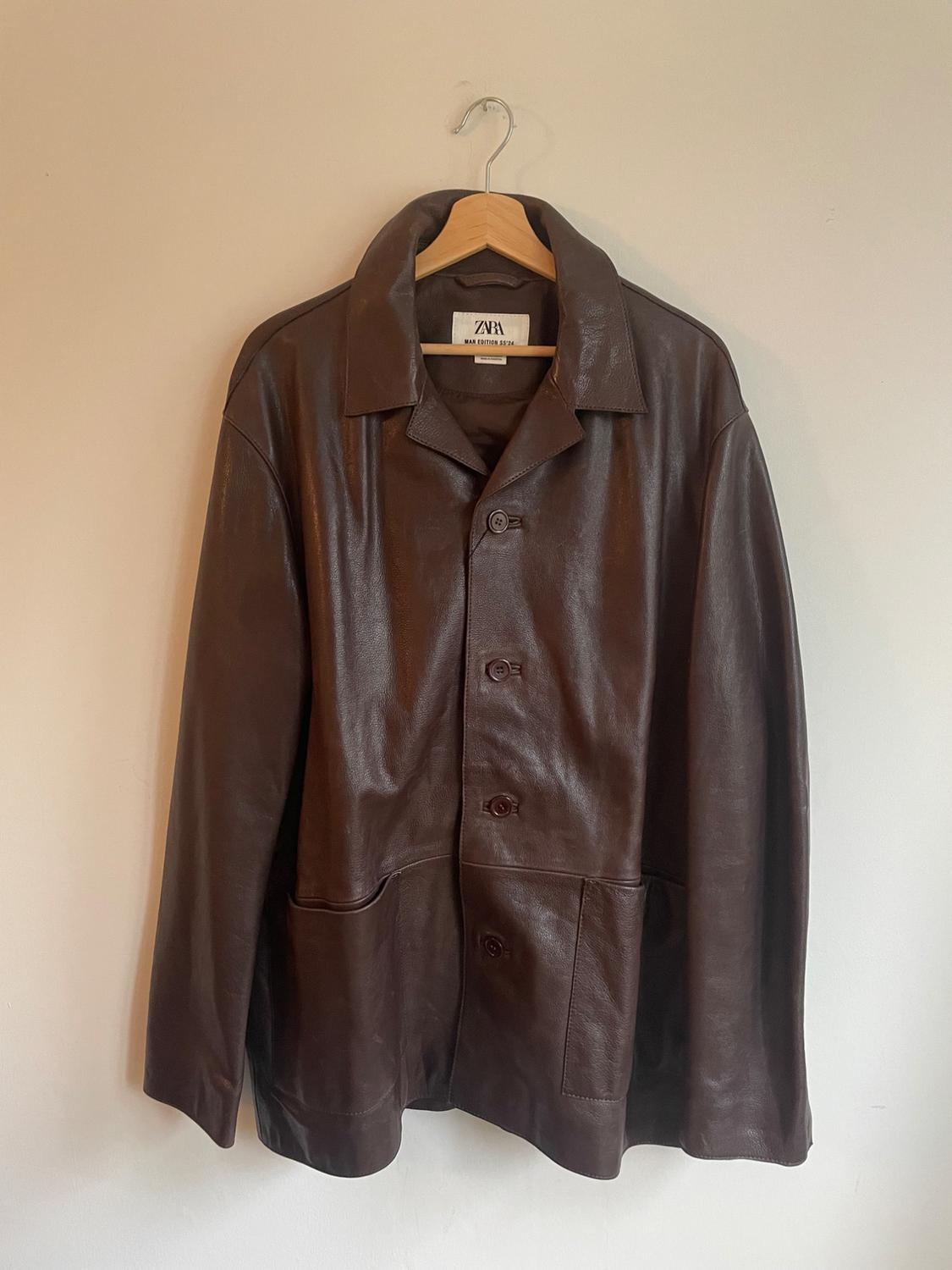 Brown leather jacket hanging on a wooden hanger. Visible label with the text "ZARA MAN EDITION 1975".