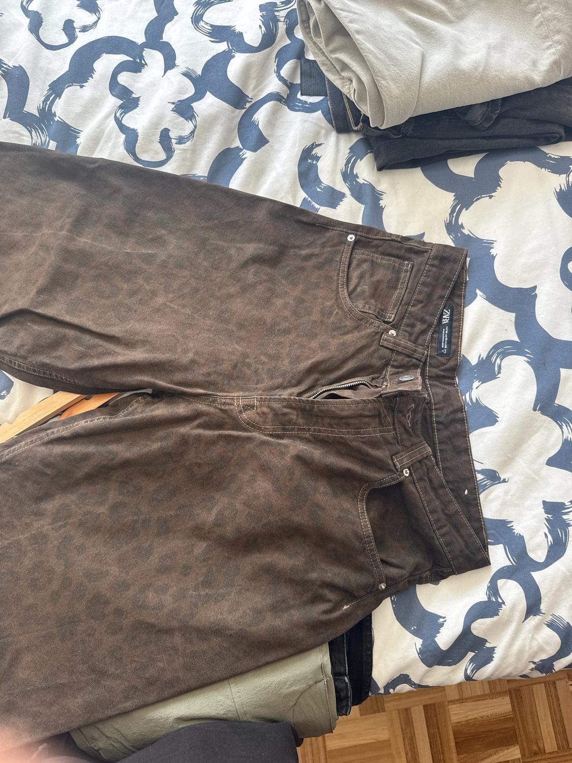 Καφέ παντελόνι με animal print πάνω σε κρεβάτι με μπλε και λευκά σεντόνια με σχέδια. Η ετικέτα ZARA είναι ορατή στη μέση.