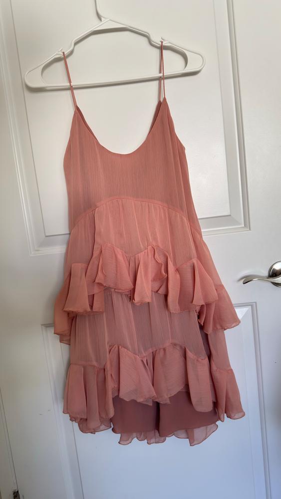 Light pink dress with thin straps and ruffles, hanging on a white hanger over a white door.