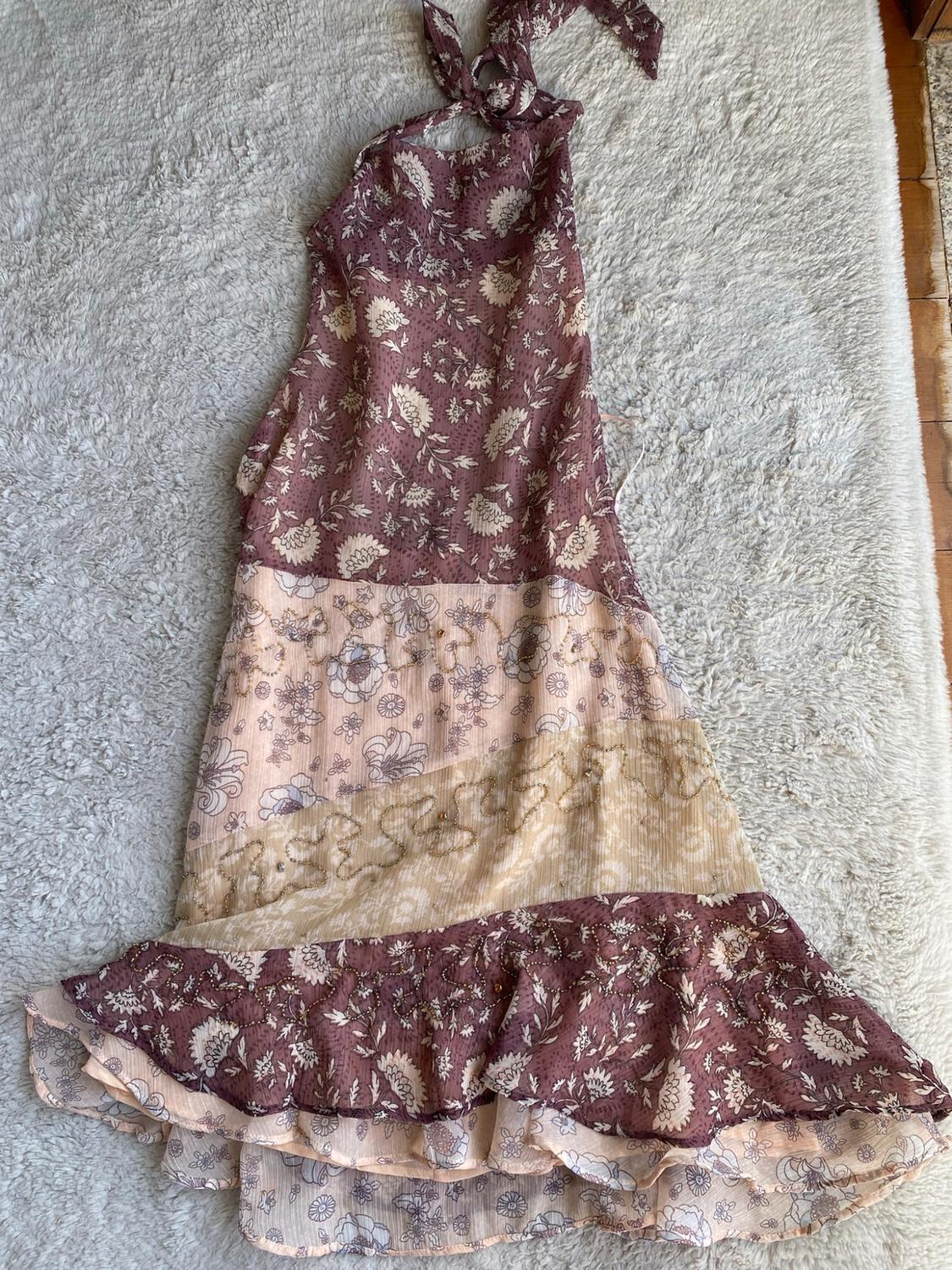 Halter dress with a floral print in mauve and beige tones, panels, embroidery and a ruffled hem on a white carpet.