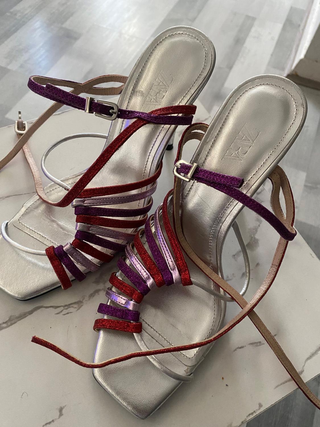 Detail of silver sandals with multicoloured straps and buckles.