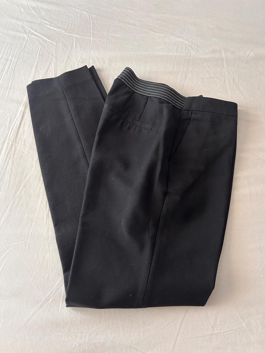 Black trousers folded on creased white fabric. Featuring an elasticated back waistband with white stripes. Relaxed style.