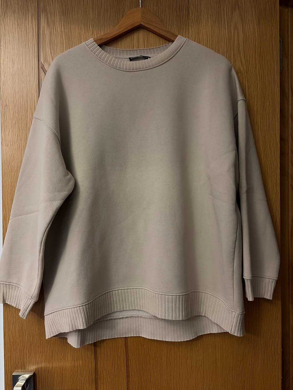 Beige long-sleeved sweatshirt hanging on a wooden hanger over a wooden door.