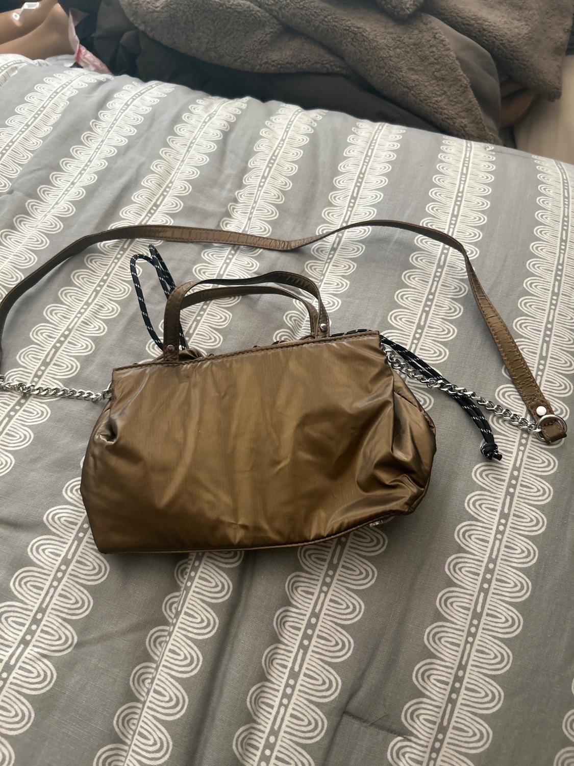 Brown bag with a long strap and short handles on a grey bedspread with a white pattern.