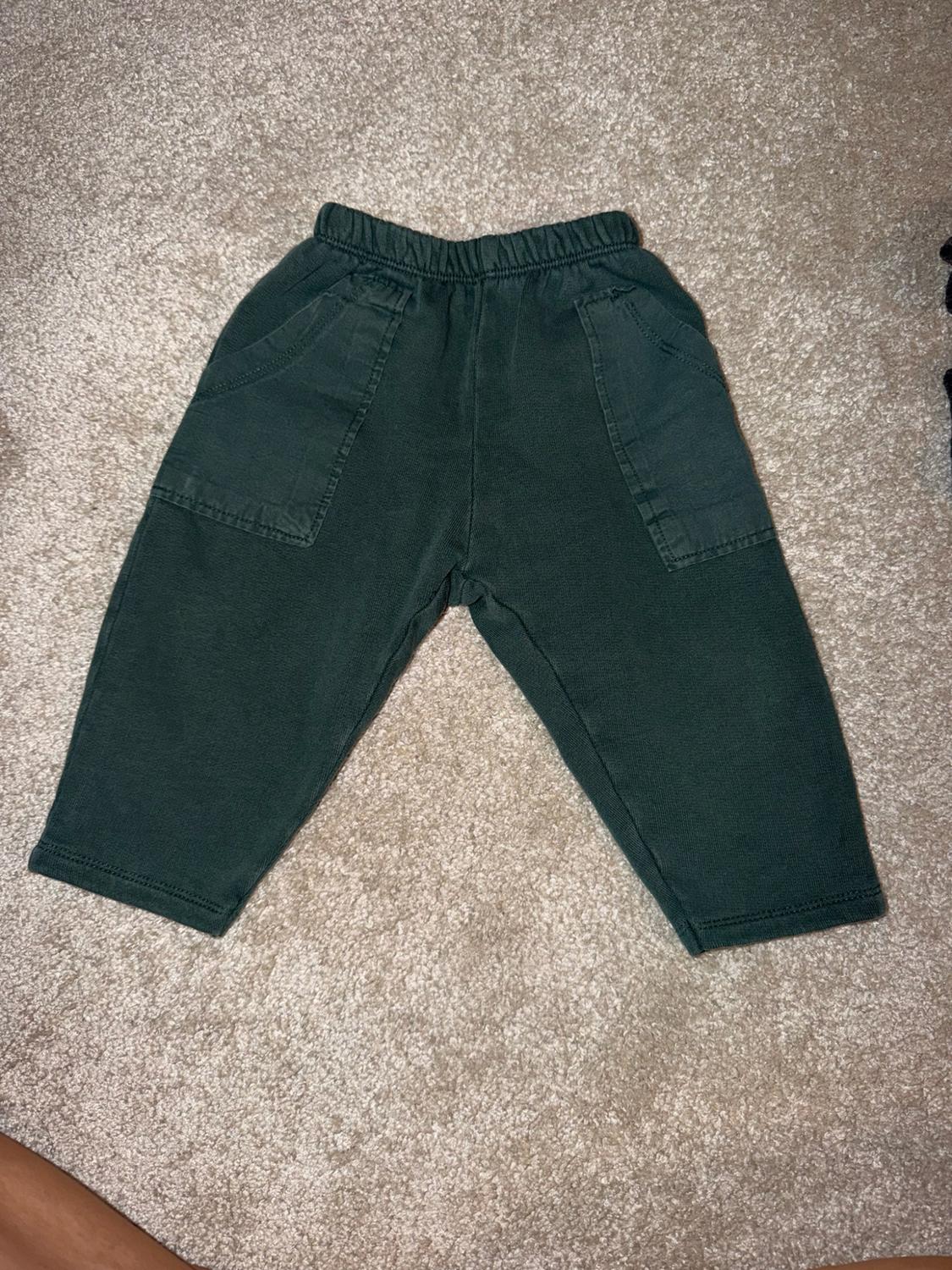Dark green trousers with an elasticated waistband and front pockets, in a relaxed composition on a beige rug.