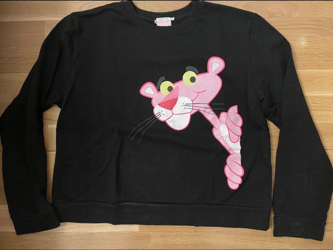 Black sweatshirt with a pink panther design on the front, on a light wooden floor.