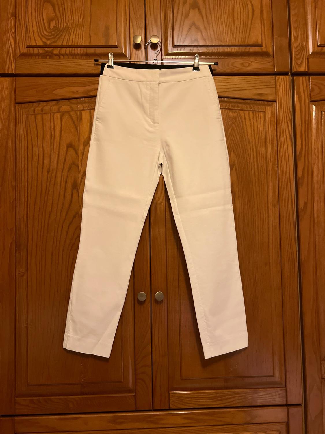 White trousers hanging on a metal hanger on wooden wardrobe doors. Casual style in a homely setting.