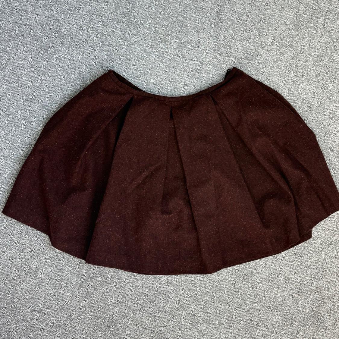 Dark brown pleated short skirt with a flared hem, spread over a gray rug.