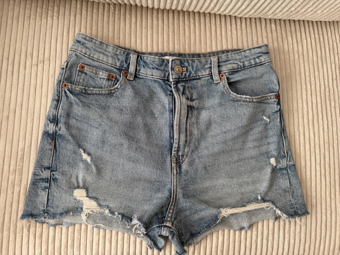 Light blue denim shorts with distressed details and a frayed hem, on a ribbed fabric surface.