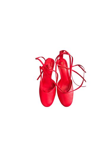 Top view of red flat shoes with a round toe and long ankle ties, on a minimalist white background.