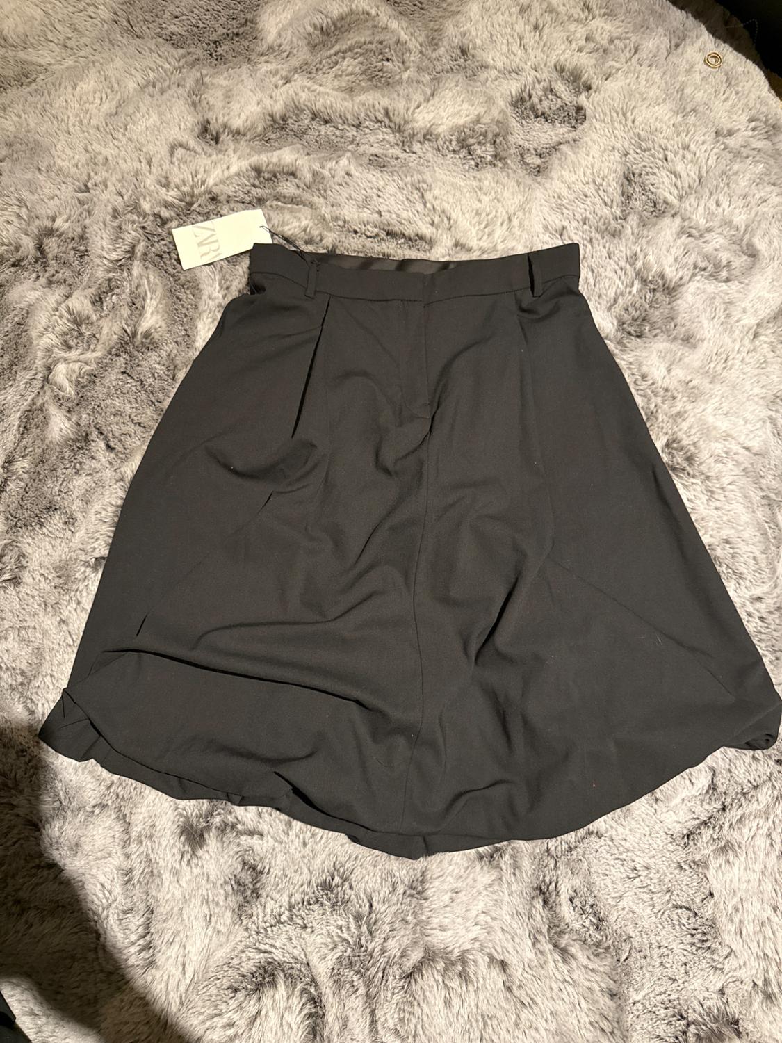 Black skirt on a fluffy gray blanket, with a white label visible at the waist.
