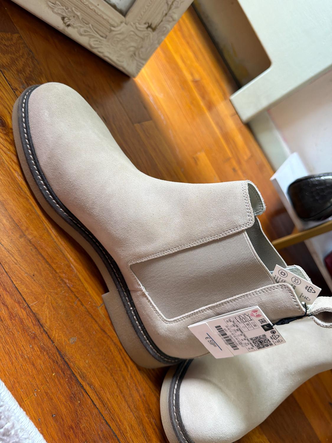 Light beige suede Chelsea boot with side elastic and a label reading "€ 59.95", on a wooden floor.