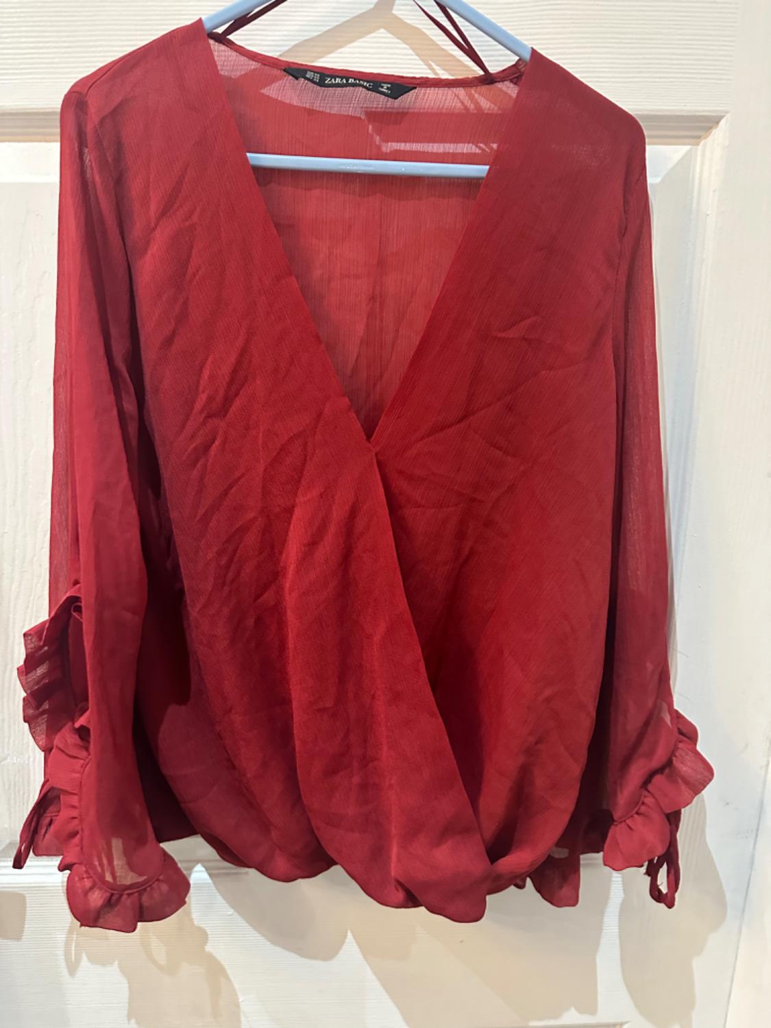 Front view of a red blouse with a V-neck and long, ruffled sleeves.