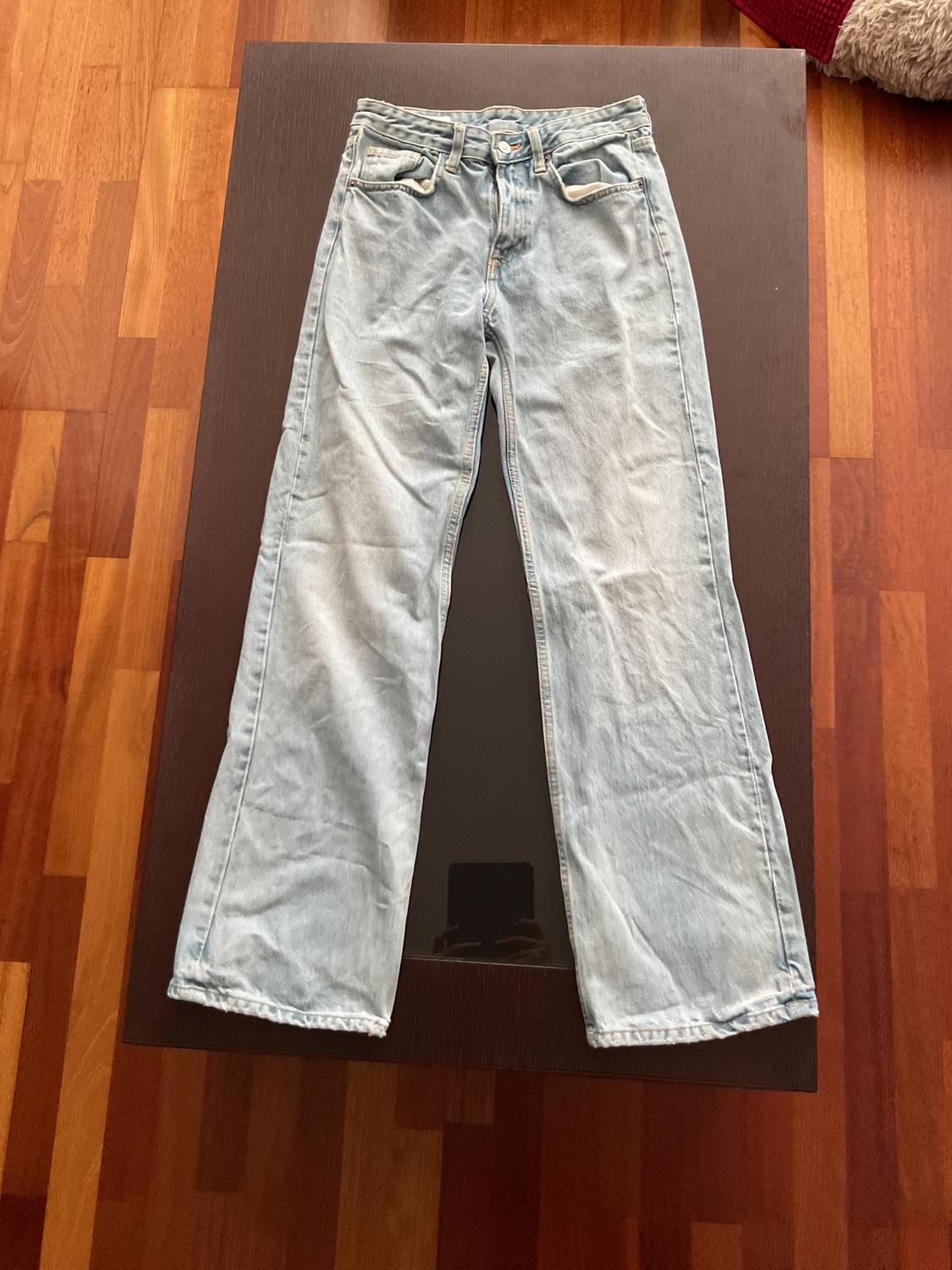 Light blue denim jeans laid out on a dark wooden table, with parquet flooring visible around.
