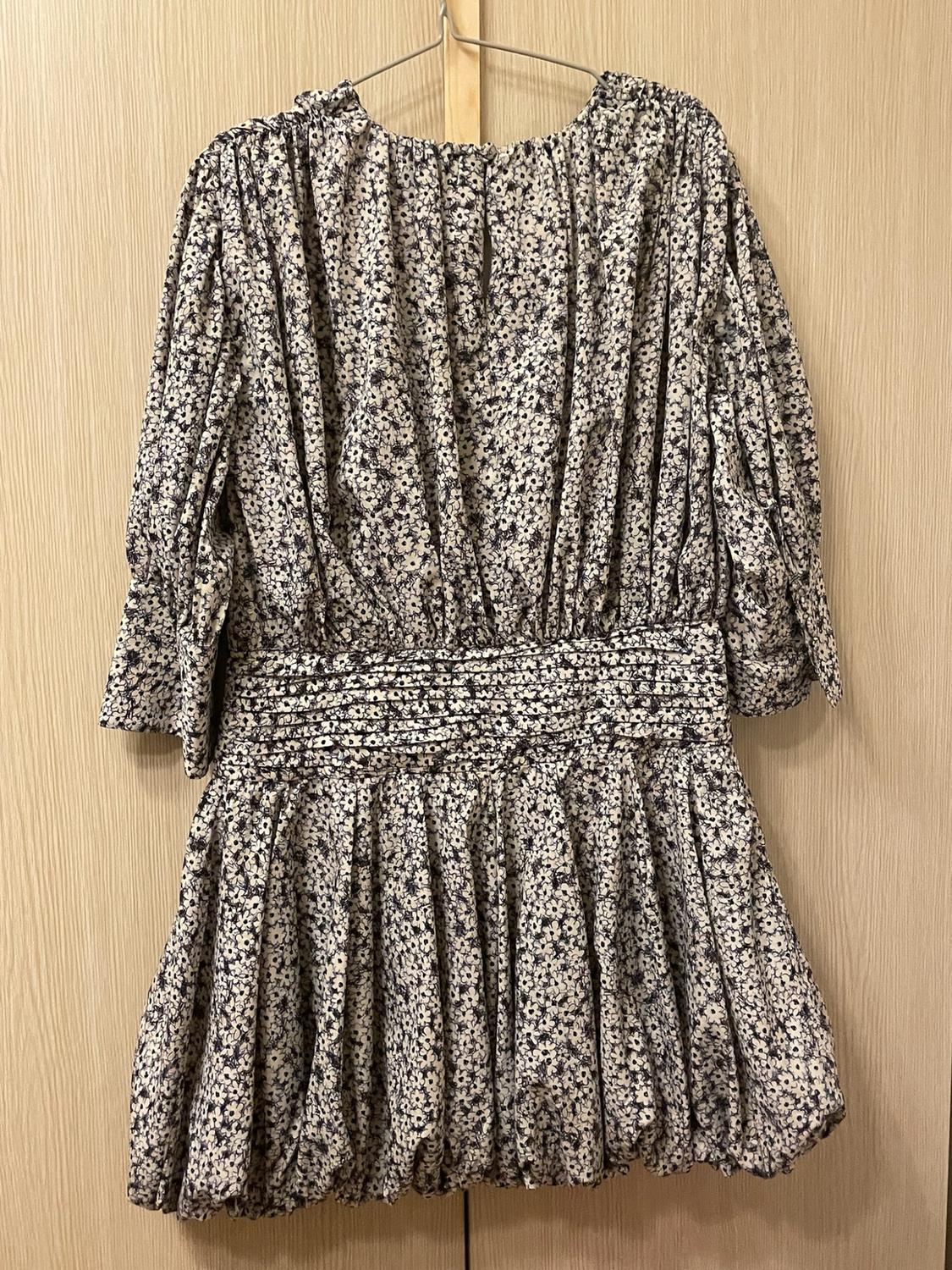 Short dress with a floral print, three-quarter-length sleeves, a gathered waist and a full skirt, hanging on a hanger against a wooden background.