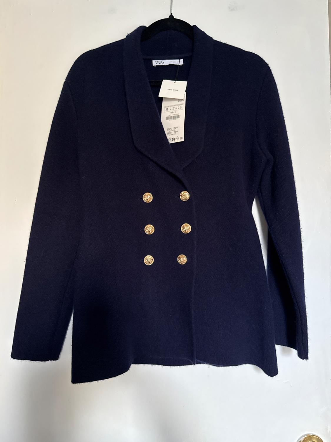 Navy blue jacket with gold buttons in two rows, hanging on a black hanger. Visible tag with size and price details.