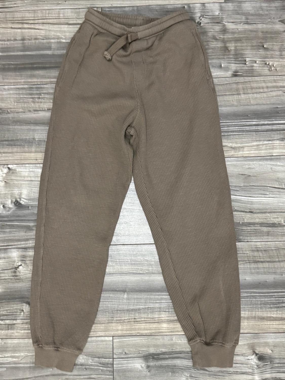 Brown jogger trousers with a waffle texture, elasticated waist, adjustable drawstring and ankle cuffs, against a grey wooden background.