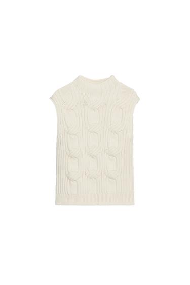 Front view of a raw knit gilet with a funnel neck and sleeveless armholes, featuring a cable knit structure.