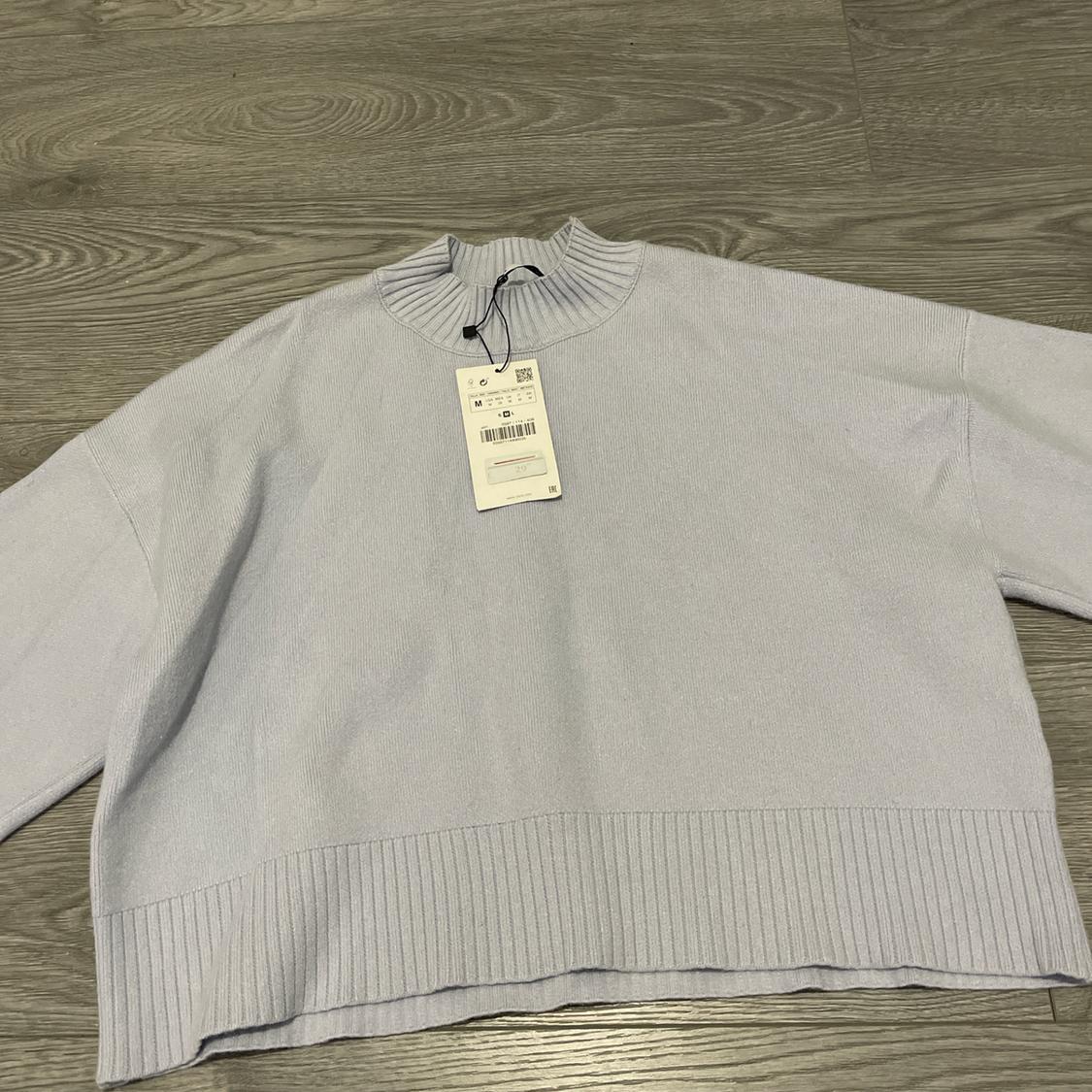 Light grey jumper with ribbed roll neck and swing tag on a grey wooden floor.