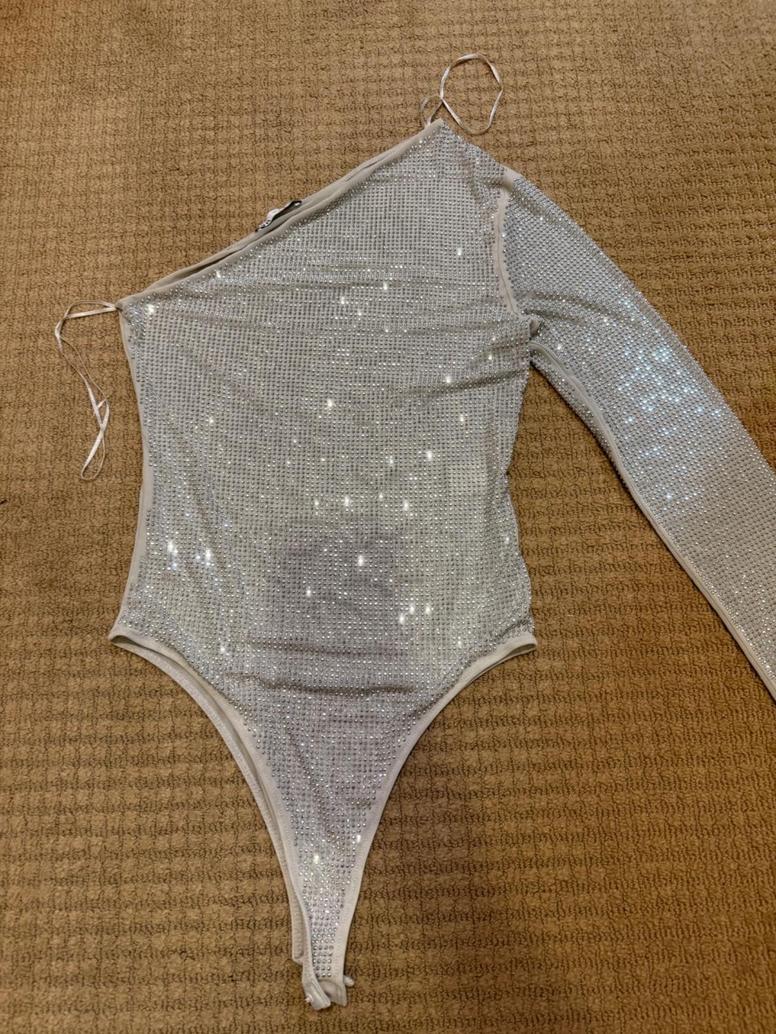 One-sleeve bodysuit with shiny silver sequins on a beige carpet. Asymmetrical design with thin straps.