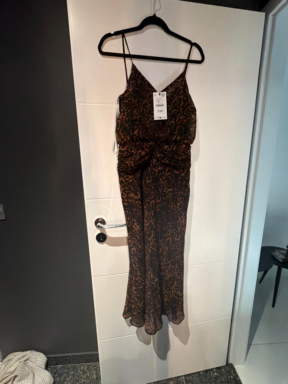 Vestido de tirantes con estampado animal colgado en una puerta blanca. Etiqueta visible en el centro del vestido.