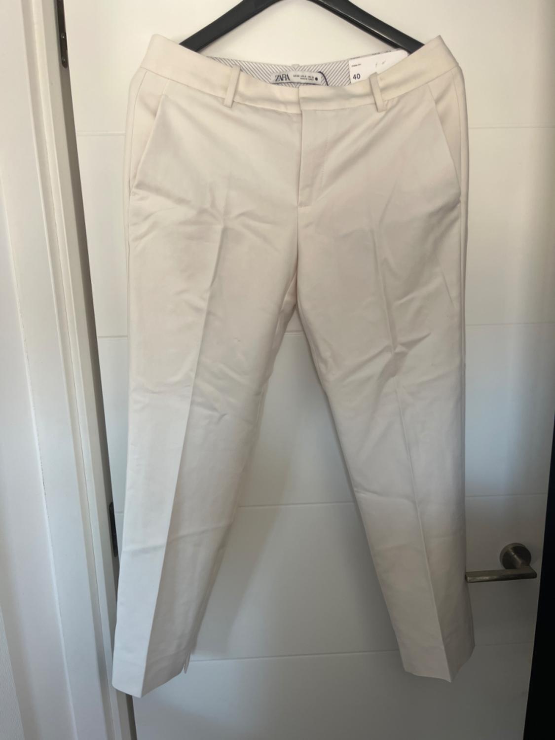 Front view of beige trousers with side pockets and belt loops.