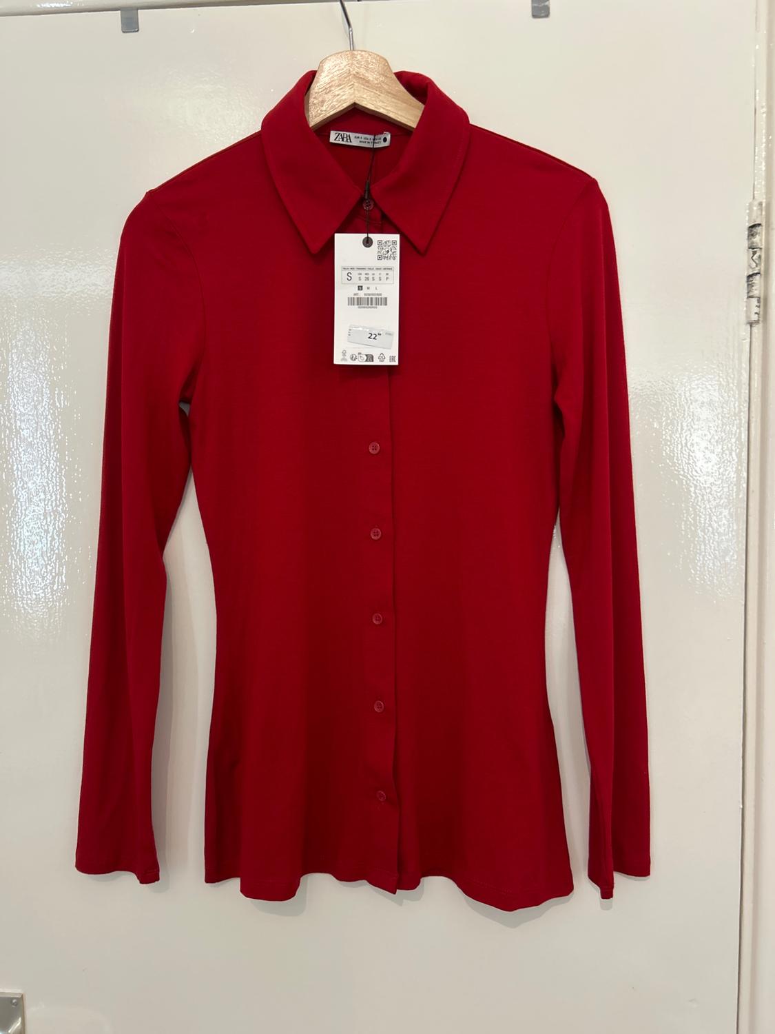 Red long-sleeved shirt hanging on a wooden hanger, with a visible price tag of €22. White background.