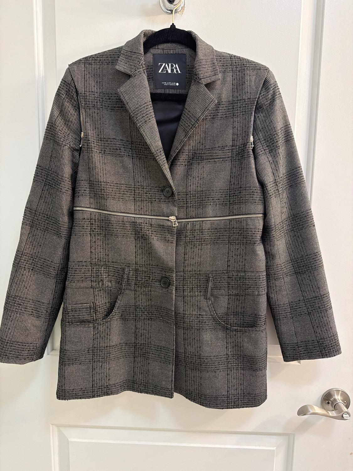 Gray jacket with a plaid print, hanging on a white door. Visible tag with the text "ZARA".