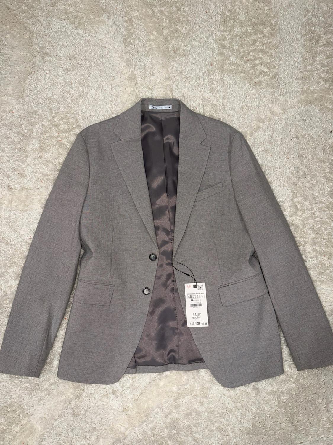 Grey jacket on a white carpet. Shows dark lining, a ZARA label and a price tag displaying the text 46, US $139 and UK £89.