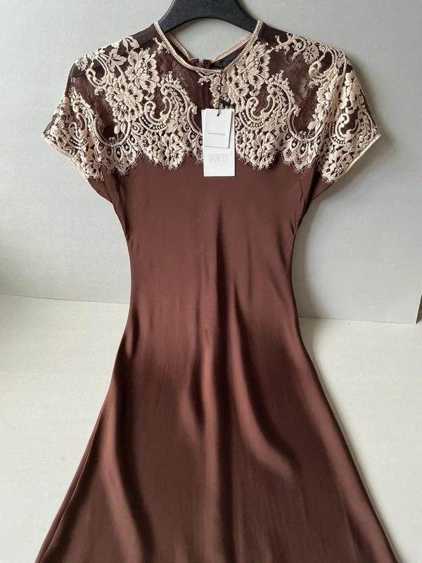 Brown dress with beige lace on the top, hanging on a black hanger. White label visible in the centre.
