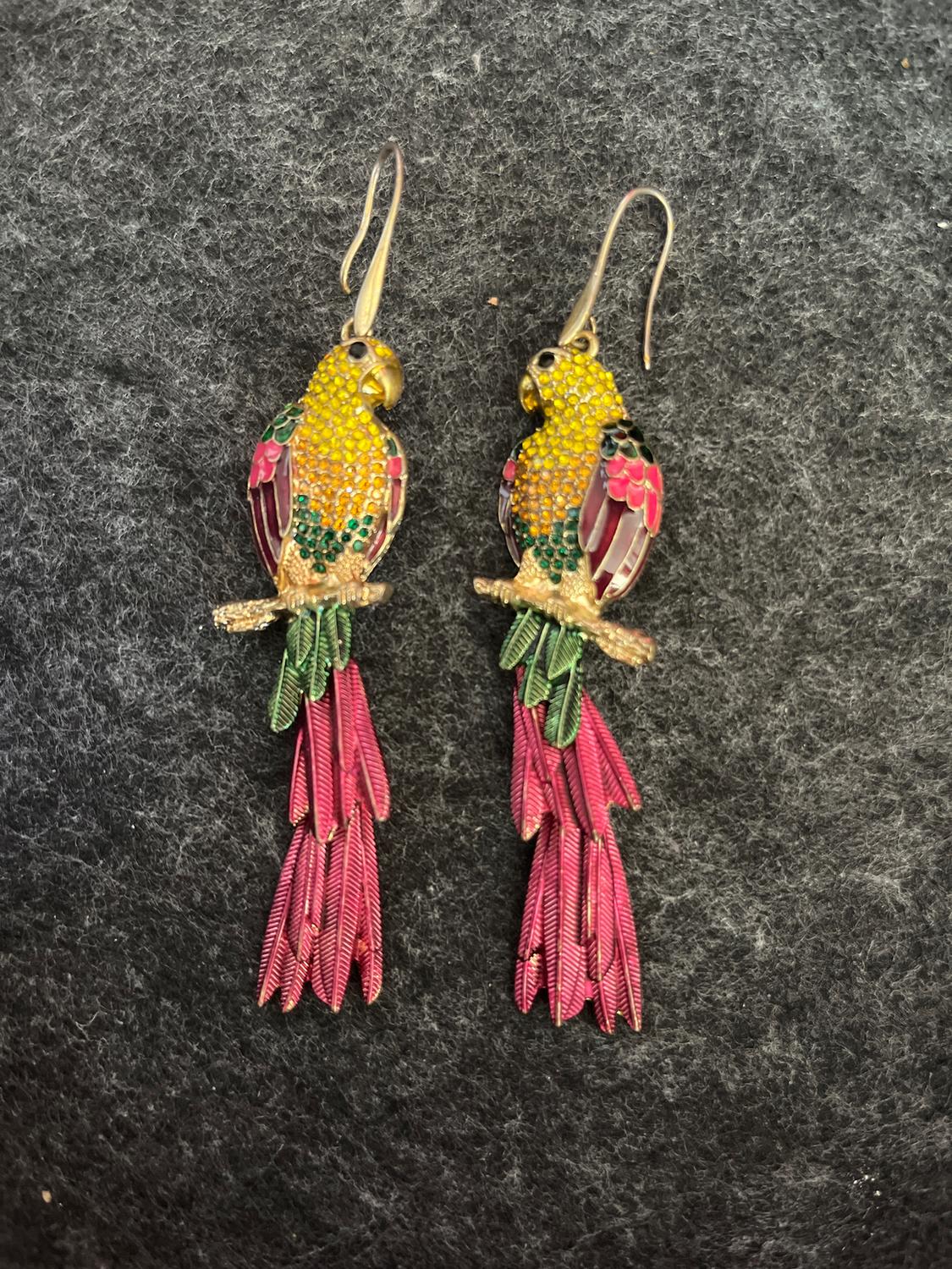 Parrot-shaped earrings with yellow, green, and pink details on a dark grey background.
